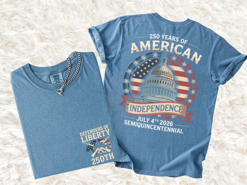 May include: Two blue t-shirts. One is folded with a silver chain necklace. The other shirt has a graphic on the back that says "250 Years of American Independence" with the Capitol building and the date July 4th 2026.