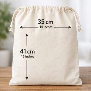 May include: A beige drawstring bag, 14 inches wide and 16 inches tall, with measurements in both inches and centimeters. The bag is made of a soft, natural fabric and sits on a wooden surface.