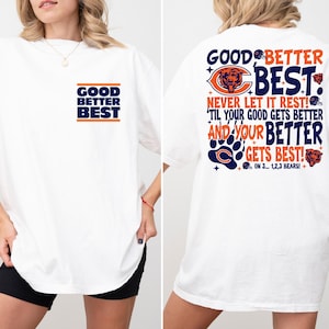 Può includere: T-shirt bianca con la scritta "GOOD BETTER BEST" in un design blu navy e arancione sul davanti. Il retro della maglietta presenta la scritta "GOOD BETTER BEST" con un logo a forma di orso e la frase "NEVER LET IT REST!"