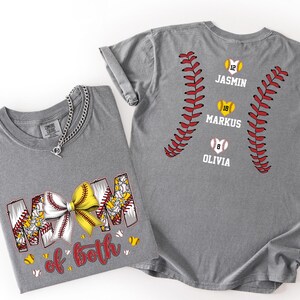 Pu&ograve; includere: Una t-shirt grigia con una grafica che riporta il testo MOM of both e un fiocco a tema baseball giallo e bianco. Il retro della maglia mostra due motivi di cuciture da baseball rosse, tre palline a forma di cuore e i nomi JASMIN, MARKUS, OLIVIA.