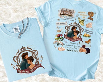 May include: Two light blue t-shirts with romantic illustrations. One shirt features a couple in a frame with the text "WE ARE ALL FOOLS IN LOVE." The other shirt has various illustrations and text, including "I LOVE YOU."