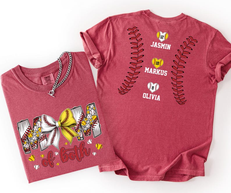 Pu&ograve; includere: Una t-shirt rossa con una grafica che riporta il testo "MOM of both" e un fiocco giallo e bianco. Il retro della maglietta mostra due motivi curvi di cuciture da baseball, tre icone di baseball a forma di cuore con i numeri 12, 18 e 8, e i nomi "JASMIN", "MARKUS" e "OLIVIA".