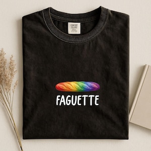 May include: Black t-shirt with a rainbow-colored baguette graphic and the word "Faguette" in white. The shirt is made of a soft material and has a classic crew neck.