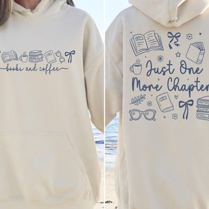 May include: Cream-colored hoodie with a front pocket and a hood. The front features the text "books and coffee" with illustrations of books, a coffee cup, and bows. The back displays the text "Just One More Chapter" with book-themed graphics.