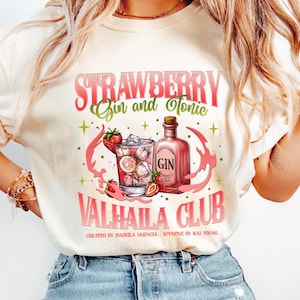 May include: Cream-colored t-shirt featuring a graphic of a strawberry gin and tonic cocktail. The design includes a cocktail glass, a gin bottle, strawberries, and the text "STRAWBERRY Gin and Tonic VALHALLA CLUB".