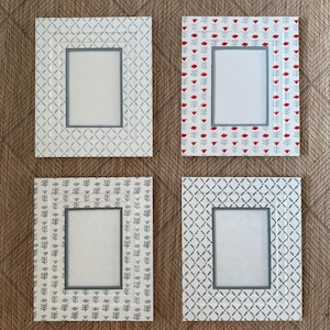 May include: Four rectangular picture frames with patterned designs. Two frames have a white background with gray geometric patterns, one with red floral accents, and one with gray floral patterns. Each frame has a gray border.