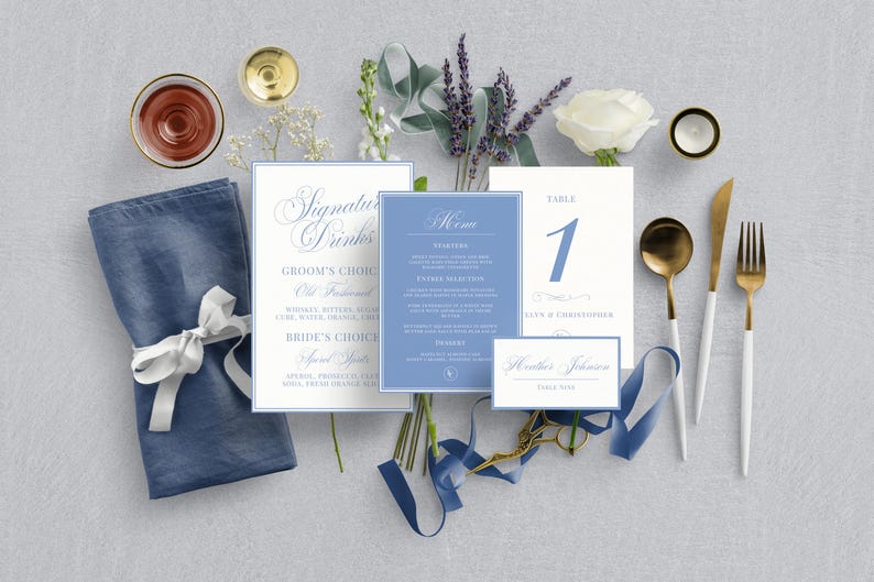 May include: A flat lay of wedding stationery and table settings in shades of blue, white, and gold. Includes menu cards, place cards, a napkin, and silverware. The table number card displays the number 1. The overall theme is elegant and classic.