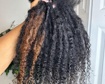 May include: A close-up of two bundles of curly hair extensions. One bundle is black and the other is a light brown color.