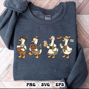 May include: A navy blue sweatshirt featuring a whimsical illustration of four cartoon ducks dressed in traditional Bavarian attire. Each duck is holding items like beer, pretzels, and a sausage, with the text "PNG - SVG - EPS" at the bottom.