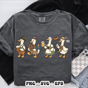 May include: Dark gray t-shirt featuring a cartoon design of four ducks dressed in traditional Bavarian attire. Each duck is holding items like beer, pretzels, and a sausage. The text "PNG - SVG - EPS" is at the bottom.
