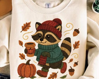Acogedor mapache otoñal PNG en estilo bordado sosteniendo un café con hojas de otoño y calabaza para sublimación en camisetas y más