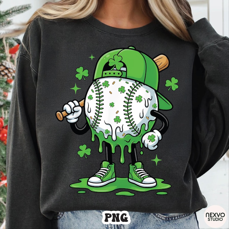 K&ouml;nnte beinhalten: Schwarzes Sweatshirt mit einer Cartoon-Baseballfigur, die eine gr&uuml;ne Kappe tr&auml;gt und einen Schl&auml;ger h&auml;lt. Der Baseball ist mit Kleebl&auml;ttern verziert, und die Figur hat gr&uuml;ne Turnschuhe und tropfenden gr&uuml;nen Schleim.