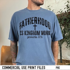 May include: A blue t-shirt with the text "FATHERHOOD IS KINGDOM WORK" and a cross graphic. The text "proverbs 22:6" is below the main text. The shirt is a solid color and has a relaxed fit.