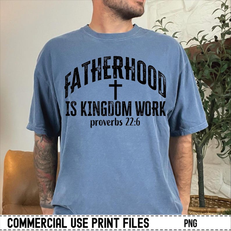 May include: A blue t-shirt with the text "FATHERHOOD IS KINGDOM WORK" and a cross graphic. The text "proverbs 22:6" is below the main text. The shirt is a solid color and has a relaxed fit.