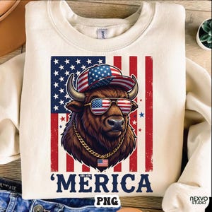 Può includere: Una felpa girocollo color crema con la grafica di un bisonte marrone che indossa un berretto da baseball e occhiali da sole con motivi della bandiera americana. Il bisonte indossa una catena d'oro con un ciondolo a bandiera. Il testo 'MERICA' appare sotto.