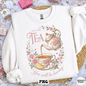 Può includere: Felpa bianca con grafica floreale a tema tè. Il design presenta una teiera che versa il tè in una tazza, circondata da fiori e la scritta "I AM THE TEA You will be having."