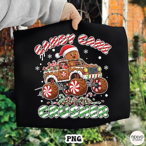 Puede incluir: Camiseta negra con un diseño festivo. Presenta un hombre de jengibre conduciendo un camión monstruo de bastón de caramelo. El texto "CANDY CANE CRUSHER" se muestra arriba y abajo del camión.