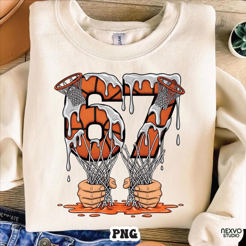 May include: Cream-colored sweatshirt featuring a basketball-themed graphic. The number "67" is designed with basketballs and dripping white paint. Two hands are holding basketball nets, with orange paint at the bottom. The word "PNG" is at the bottom.