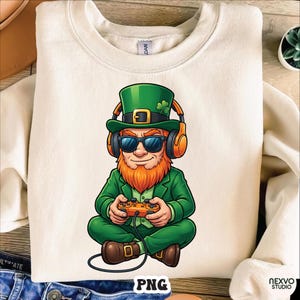 May include: Cream-colored sweatshirt featuring a cartoon leprechaun wearing sunglasses, a green hat with a shamrock, and orange headphones. The leprechaun is holding a game controller. The word "PNG" is printed at the bottom.