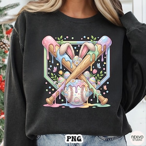 May include: Black sweatshirt with a colorful graphic featuring crossed baseball bats, a baseball, and Easter eggs. The design includes bunny ears, flowers, and pastel drips, creating a festive spring theme.