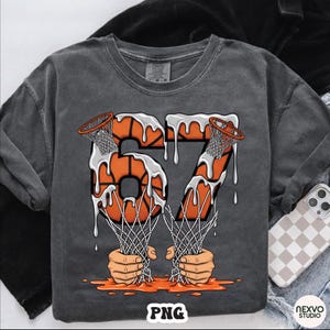 May include: Dark gray t-shirt with a basketball-themed graphic. The design features the number "67" in orange, resembling basketballs with dripping white paint. The nets are held by hands, with the word "PNG" at the bottom.