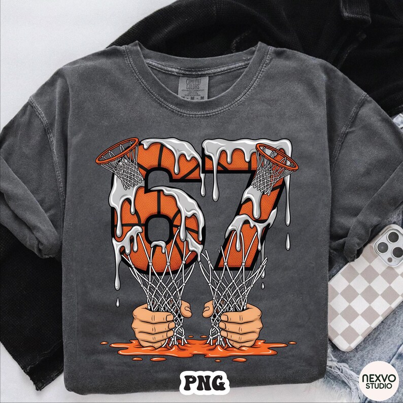 May include: Dark gray t-shirt with a basketball-themed graphic. The design features the number "67" in orange, resembling basketballs with dripping white paint. The nets are held by hands, with the word "PNG" at the bottom.