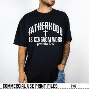May include: Black t-shirt with the text "FATHERHOOD IS KINGDOM WORK" in white, with a cross symbol and the Bible verse Proverbs 22:6. The shirt is a classic crew neck style.