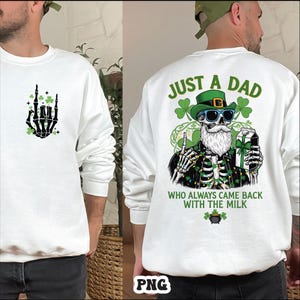 Op de afbeelding: Wit sweatshirt met een skelet hand-afbeelding en klavers op de voorkant. De achterkant toont een skelet met een groene hoed en zonnebril, met de tekst "JUST A DAD WHO ALWAYS CAME BACK WITH THE MILK."