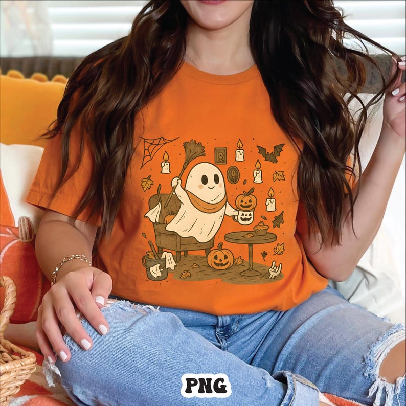 May include: Orange t-shirt featuring a cartoon ghost with a broom, holding a pumpkin-shaped mug. The design includes pumpkins, candles, bats, and a spiderweb, perfect for Halloween. The shirt is a comfortable fit.