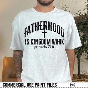 May include: A light gray t-shirt with the text "FATHERHOOD IS KINGDOM WORK" in black, with a cross symbol and the Bible verse Proverbs 22:6. The shirt is a casual wear item.