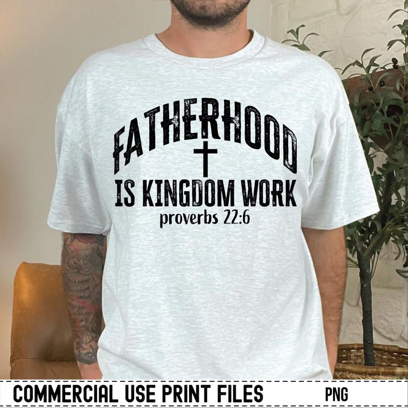 May include: A light gray t-shirt with the text "FATHERHOOD IS KINGDOM WORK" in black, with a cross symbol and the Bible verse Proverbs 22:6. The shirt is a casual wear item.