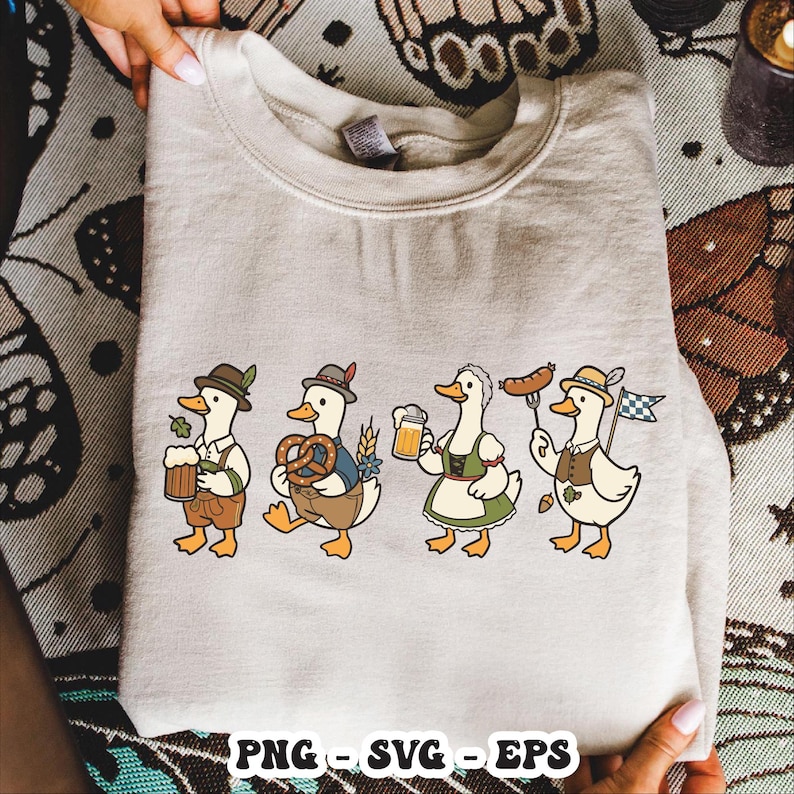 May include: A beige sweatshirt featuring a cartoon design of four ducks dressed in traditional Bavarian attire. Each duck is holding items like beer, pretzels, and sausages. The bottom of the sweatshirt has the text "PNG - SVG - EPS".