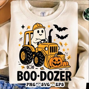 May include: Cream-coloured sweatshirt with a Halloween-themed graphic. The design features a ghost driving a yellow bulldozer with a pumpkin bucket, the text "BOO-DOZER", bats, stars, and pumpkins. The bottom of the shirt has the text "PNG SVG EPS".