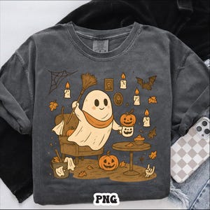 May include: Dark gray long-sleeve shirt with a Halloween-themed graphic. The design features a friendly ghost holding a broom and a cup of coffee, surrounded by pumpkins, candles, and autumn leaves. The word "PNG" is at the bottom.