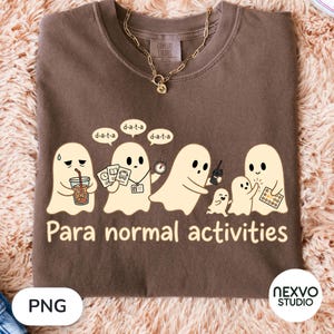 Peut inclure: Un t-shirt marron avec un motif représentant cinq fantômes couleur crème. Les fantômes tiennent des objets comme une boisson, des cartes, un chronomètre et un talkie-walkie. Au-dessus, des bulles portent le texte d-a-t-a. En bas, le texte Para normal activities.