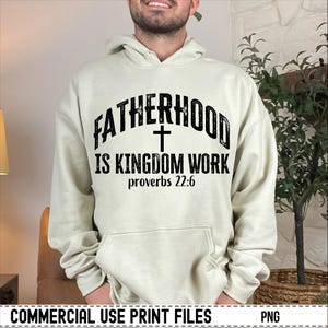 May include: A cream-colored hoodie with the text "FATHERHOOD IS KINGDOM WORK" in black, with a cross symbol and the Bible verse Proverbs 22:6. The hoodie has a drawstring hood and a front pocket.