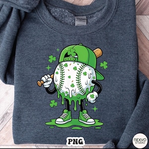 K&ouml;nnte beinhalten: Dunkelgraues Sweatshirt mit einer Cartoon-Baseballfigur mit gr&uuml;ner Baseballkappe und Kleebl&auml;ttern. Der Baseball ist wei&szlig; mit gr&uuml;nen Kleebl&auml;ttern und tropfenden gr&uuml;nen Akzenten. Die Figur h&auml;lt einen Holzschl&auml;ger und tr&auml;gt gr&uuml;ne Turnschuhe.