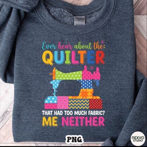 May include: A dark gray sweatshirt with a colorful graphic design. The design features a sewing machine made of patchwork fabric and the text "Ever hear about the: QUILTER THAT HAD TOO MUCH FABRIC? ME NEITHER."