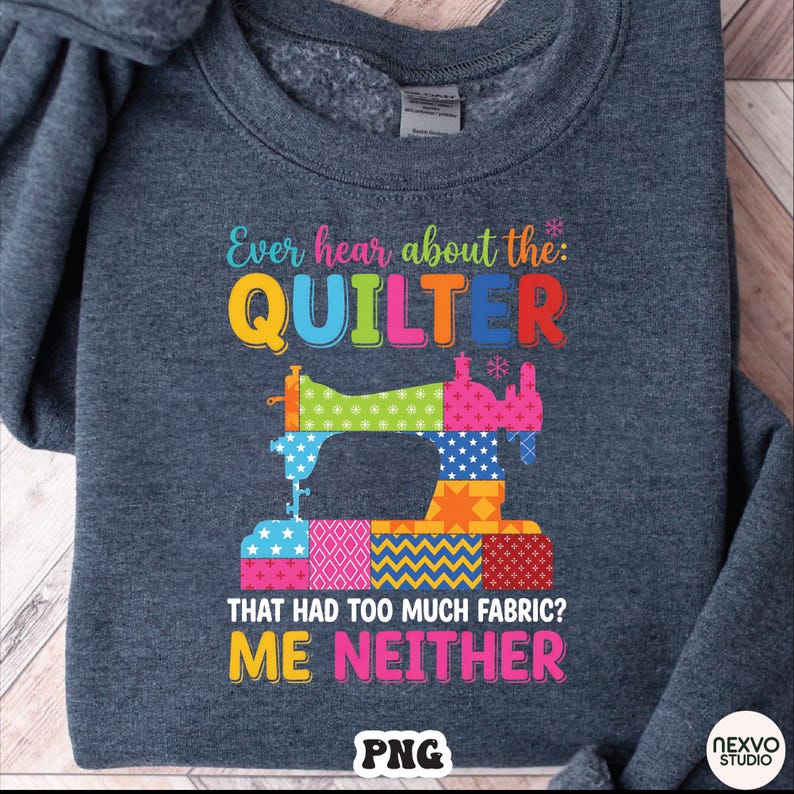 May include: A dark gray sweatshirt with a colorful graphic design. The design features a sewing machine made of patchwork fabric and the text "Ever hear about the: QUILTER THAT HAD TOO MUCH FABRIC? ME NEITHER."