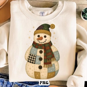 May include: Cream-colored sweatshirt featuring a patchwork snowman design. The snowman wears a green and brown hat, a plaid scarf, and has button details. The design includes a carrot nose and a smiling face. Gold star accents surround the snowman.