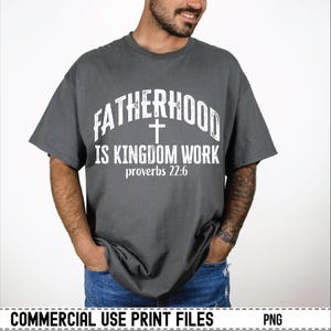 May include: A gray t-shirt with the text "FATHERHOOD IS KINGDOM WORK" in white, along with a cross and the Bible verse Proverbs 22:6. The shirt is a casual style, suitable for everyday wear.