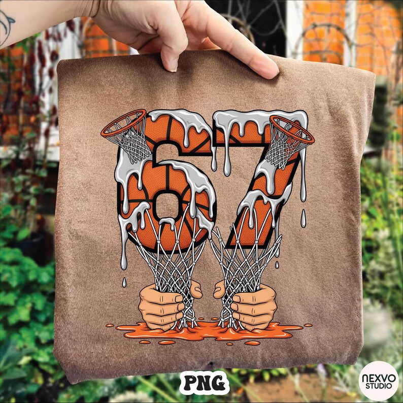 May include: A brown t-shirt featuring a basketball-themed graphic. The number "67" is designed with basketballs and nets, with a dripping effect. The bottom of the graphic shows two hands holding the nets. The bottom right corner has the text "NEXVO STUDIO".