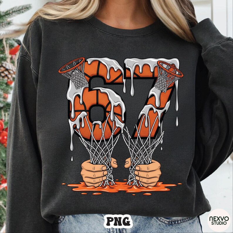 May include: Dark gray sweatshirt featuring a basketball-themed graphic. The design includes the number "67" formed by basketballs with dripping white paint, basketball nets, and hands holding the nets. The overall design has an orange and white color scheme.