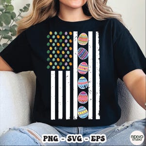 Może przedstawiać: Czarny t-shirt z motywem wielkanocnym. Grafika przypomina amerykańską flagę, z gwiazdami zastąpionymi kolorowymi pisankami, a pasami białymi liniami pionowymi. Koszulka ma krótkie rękawy.