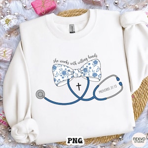 Könnte beinhalten: Weißes Sweatshirt mit blauem Blumen-Schleife, Stethoskop und Kreuz-Design. Der Text "she works with willing hands" und "PROVERBS 31:13" sind ebenfalls auf dem Shirt abgebildet.