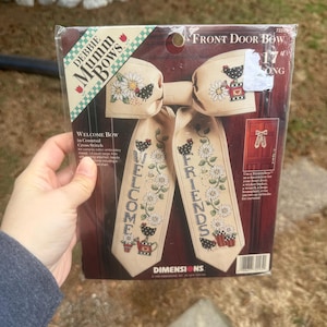 Peut inclure: Kit de point de croix pour un nœud de porte d'entrée avec le texte "WELCOME FRIENDS". Le nœud est beige avec des motifs floraux et de poulets. Le nœud mesure 43 cm de long.