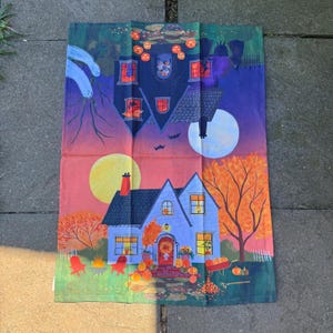 Puede incluir: Un pa&ntilde;o de cocina con tem&aacute;tica de Halloween con una ilustraci&oacute;n caprichosa de una casa embrujada y una luna llena. El dise&ntilde;o incluye calabazas, murci&eacute;lagos y una atm&oacute;sfera espeluznante, con una paleta de colores naranja, morado y azul.