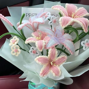 May include: A bouquet of handmade pink and white lilies, accented with green stems and delicate white and lavender butterflies. The bouquet is wrapped in light blue paper and tied with a shimmering blue ribbon. Text reads "Our bestseller".