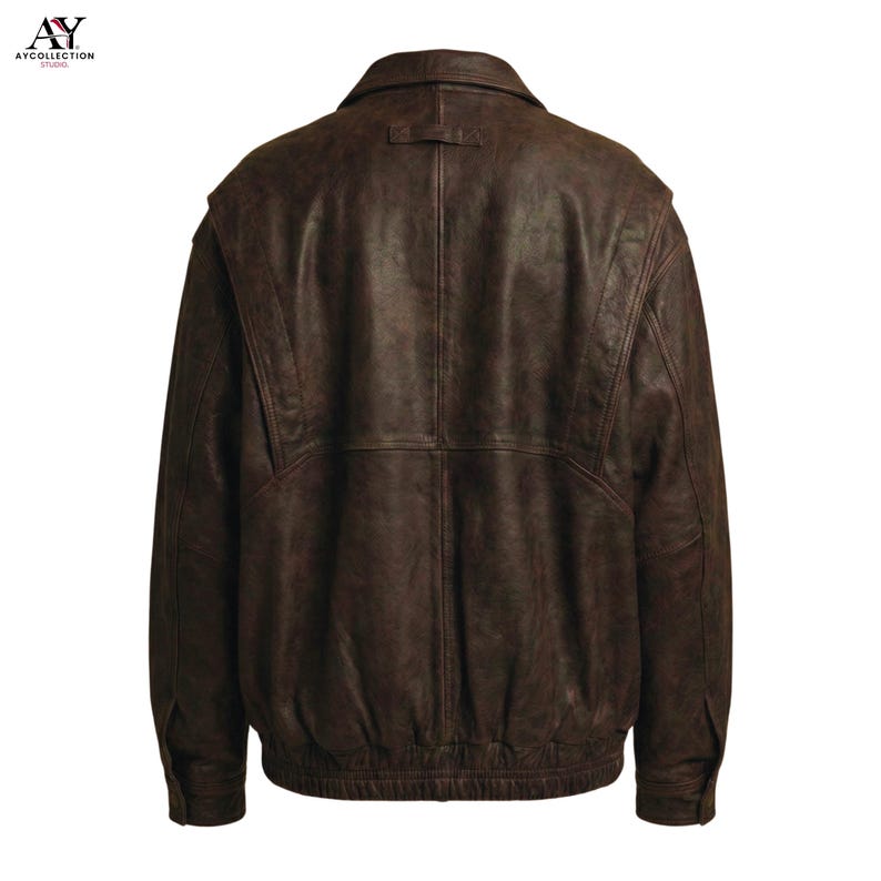 Puede incluir: Chaqueta de cuero marr&oacute;n con dise&ntilde;o tipo bomber. La chaqueta presenta un cuello, una peque&ntilde;a trabilla en la parte trasera del cuello y un dobladillo acanalado. La parte trasera de la chaqueta es visible, mostrando las costuras y los detalles de los paneles.