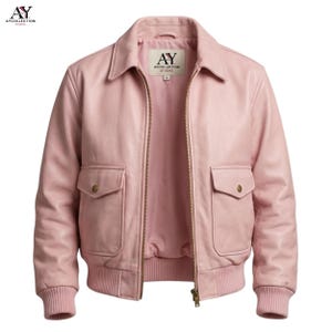 May include: A light pink leather jacket with a collared neckline, two front pockets, and a ribbed hem and cuffs. The jacket has a zipper closure and a label inside the collar that reads "AY COLLECTION STUDIO".